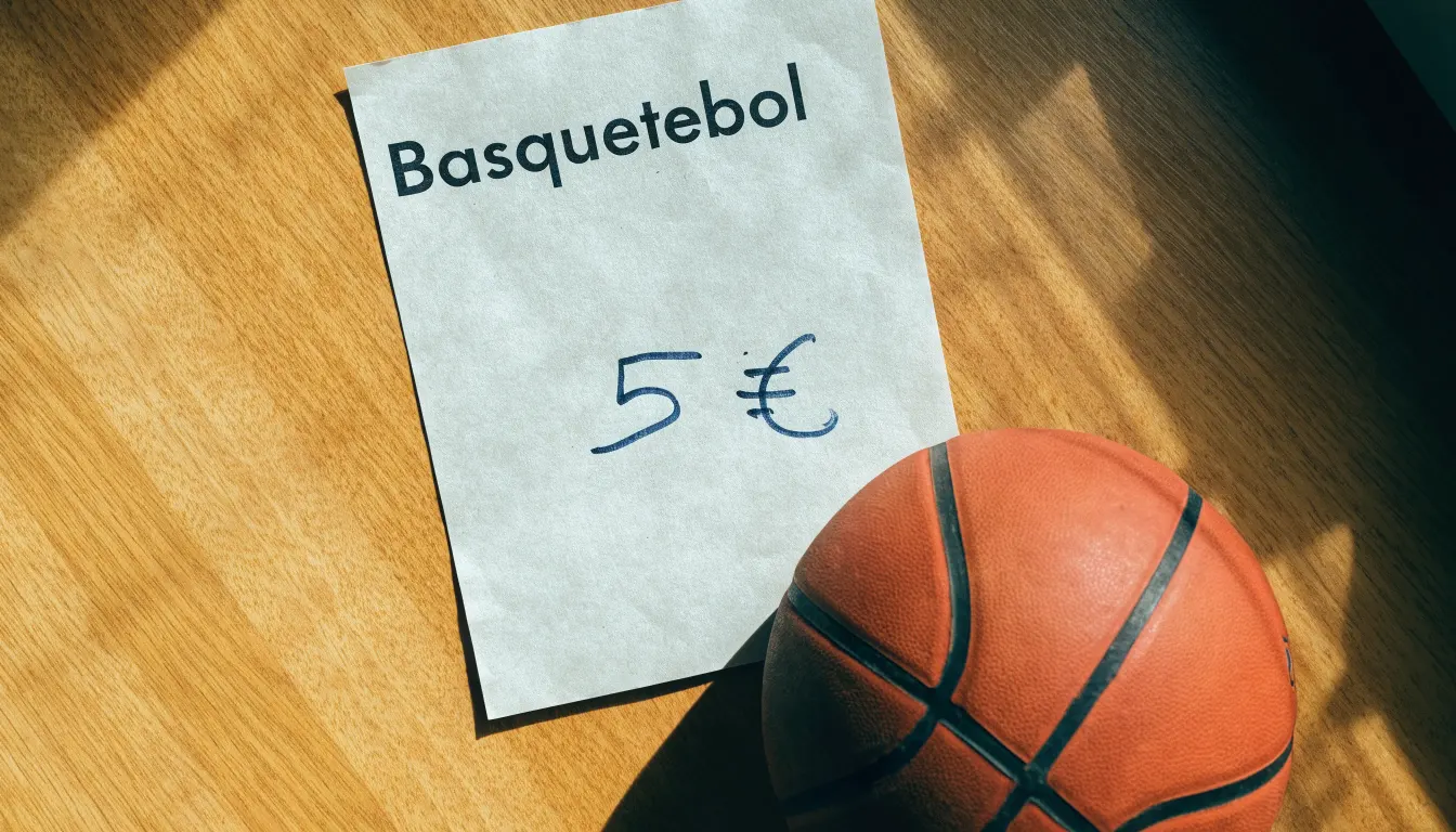 Uma bola de futebol pousada sobre um talão de apostas em branco numa mesa de madeira, à luz do dia