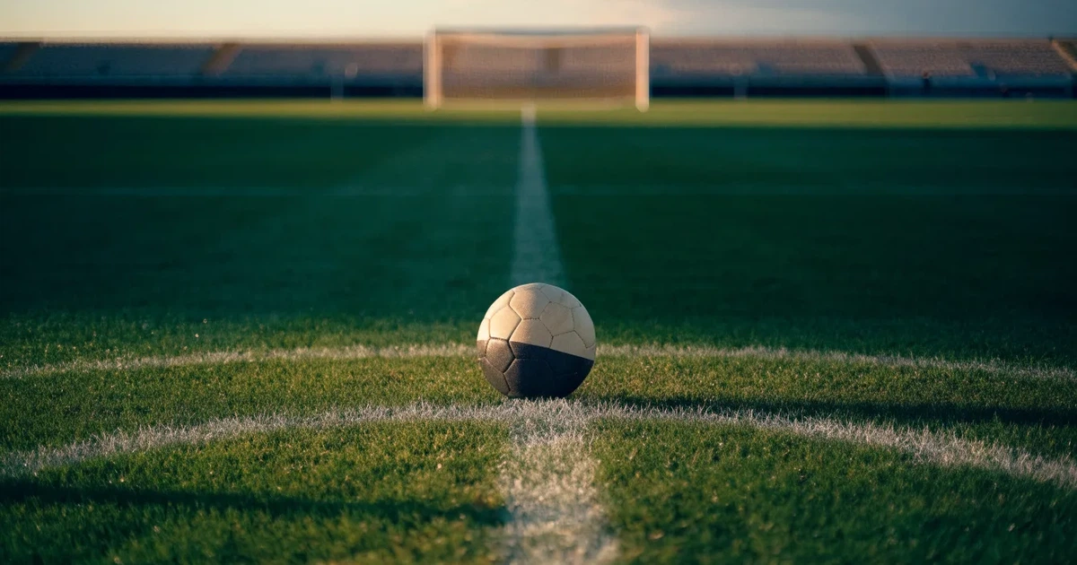 Uma bola de futebol no ponto central de um relvado, à luz da manhã