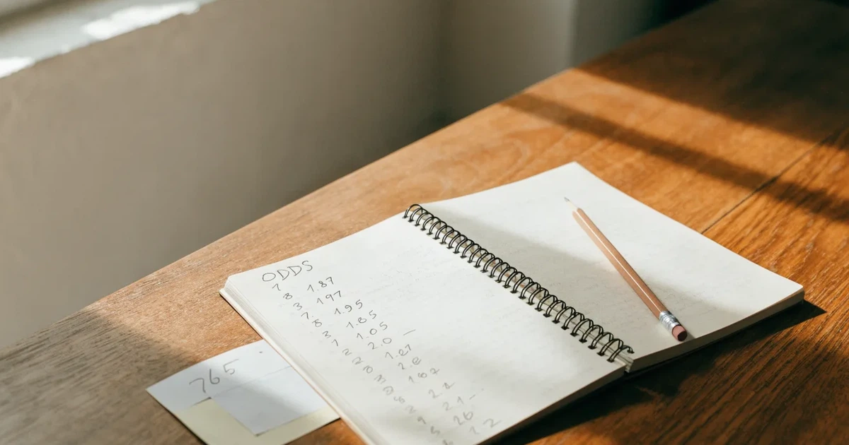 Um caderno aberto com cotas escritas à mão, uma calculadora e um lápis sobre uma mesa de madeira